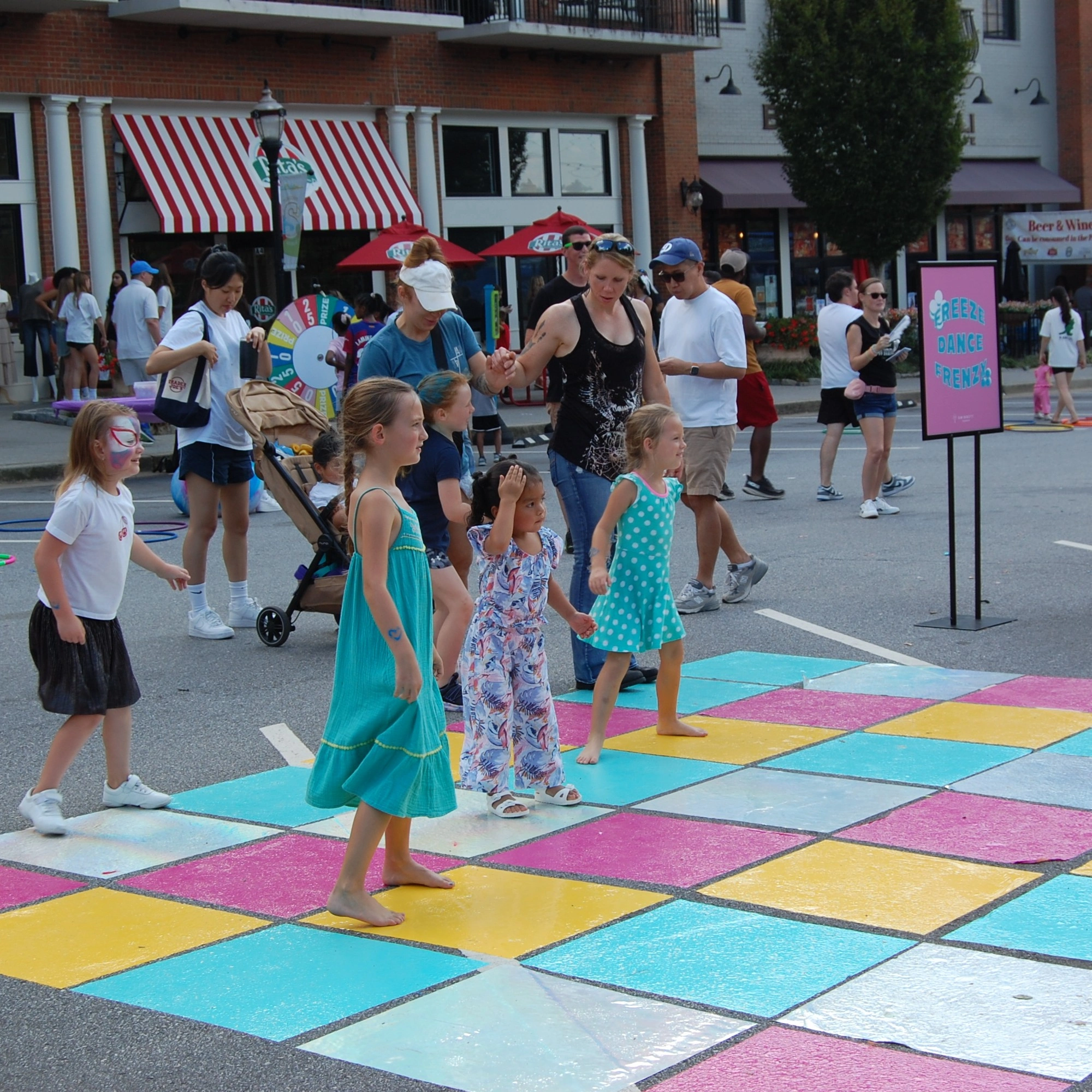 Children playing on a colorful checkerboard-painted street in the Family Fun Zone.