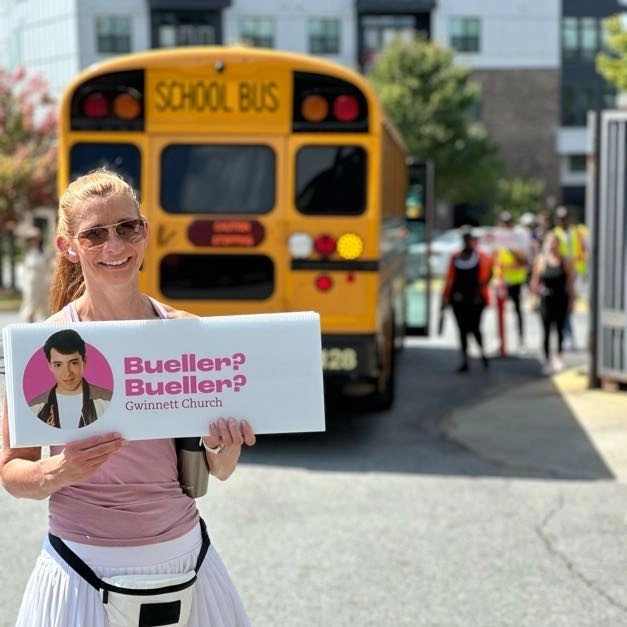 Woman holding a sign in front of a shuttle bus.