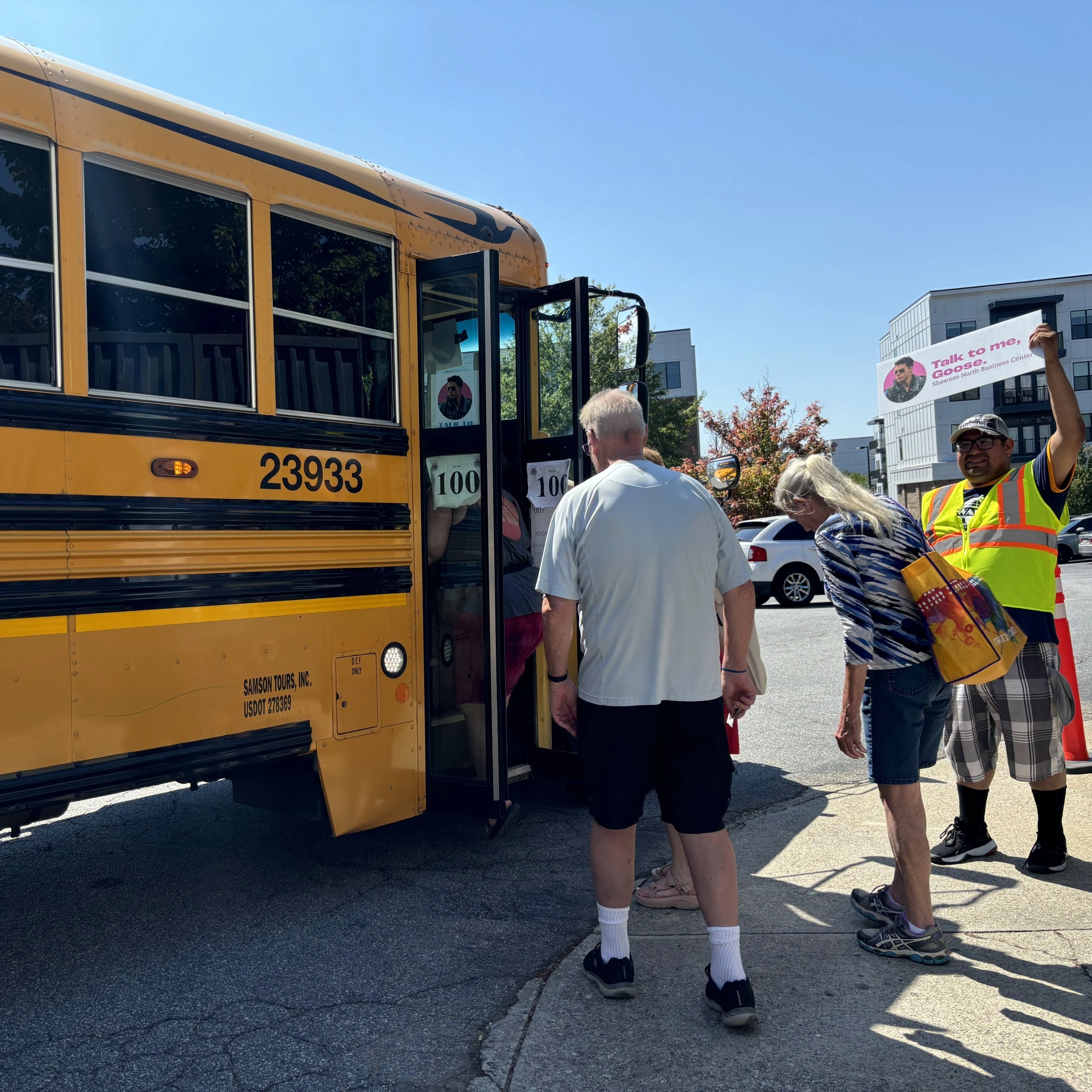 People boarding a yellow shuttle bus while a man in a safety vest holds up a sign.